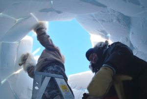 Two men inserting the final blocks of snow into the roof of an iglu