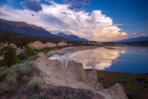 A lake with rock and plant life around it with the clouds and sky reflected