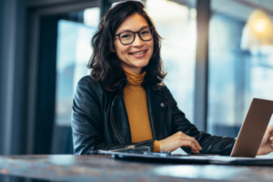 Young cheerful woman sitting at a table with a lap top.