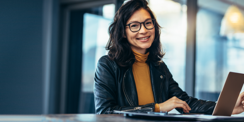 Young cheerful woman sitting at a table with a lap top.