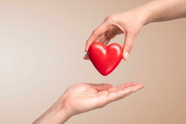 One outstretched hand placing a plastic red heart into another outstretched hand