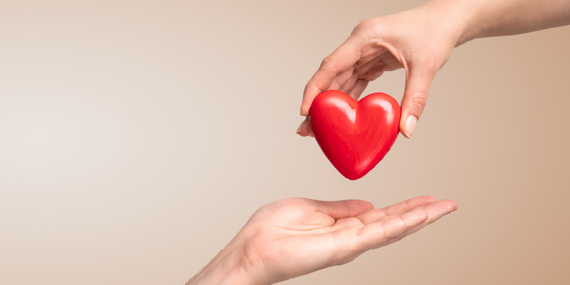 One outstretched hand placing a plastic red heart into another outstretched hand