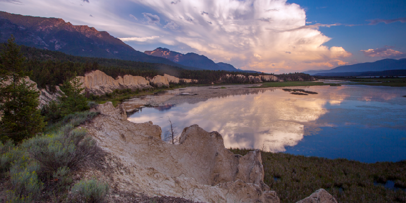 A lake with rock and plant life around it with the clouds and sky reflected