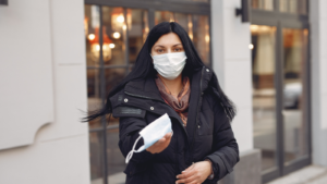 Woman wearing a mask with an outstretched hand holding out a mask to the camera man.