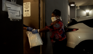 Woman wearing a mask handing off bags of groceries in a parking garage.